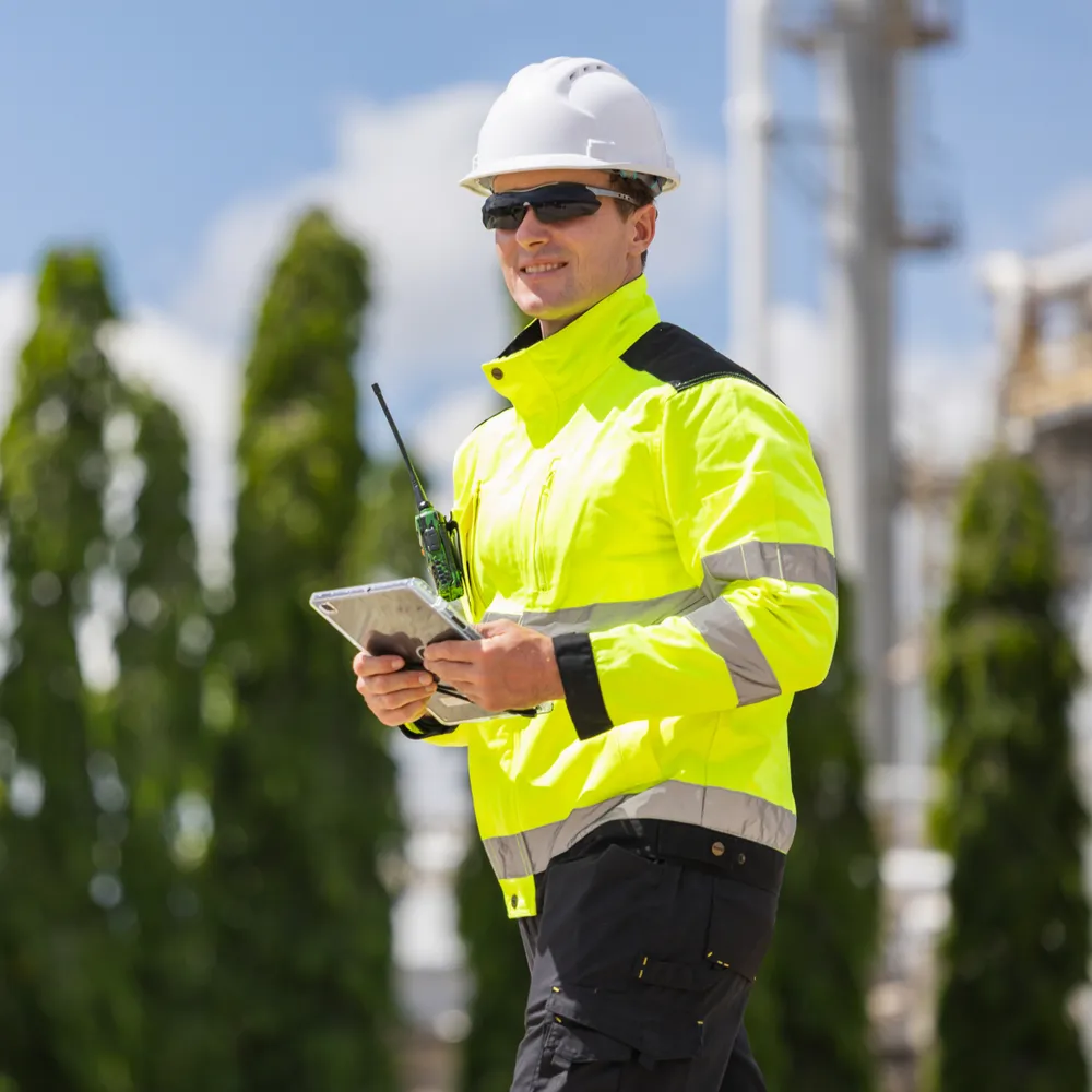 Contractor in Class 3 hi-vis yellow jacket and safety helmet checking a tablet on site